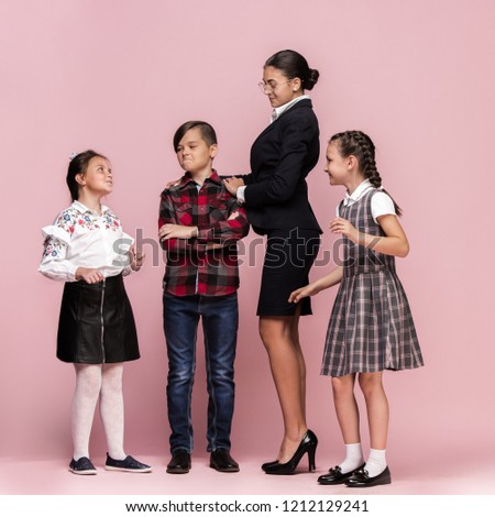 Cute smiling happy stylish children and female teacher on pink background. Beautiful stylish teen girls and boy standing together and posing at studio. Classic style. Kids fashion and emotions concept