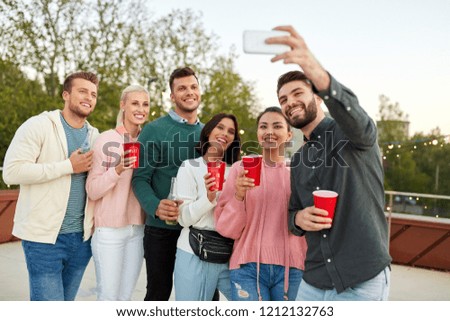 leisure and people concept - happy friends with drinks taking selfie by smartphone at rooftop party in summer