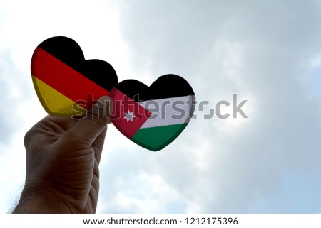 Hand holds a heart Shape Germany and Jordan flag, love between two countries