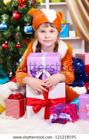 Little girl in suit of squirrels surrounded by gifts in festively decorated room