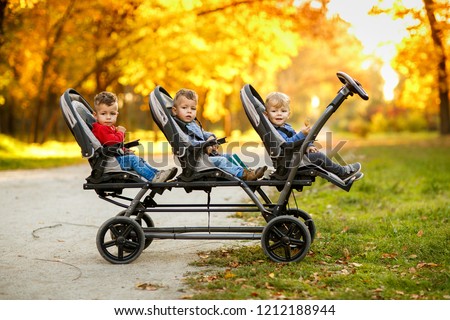 The happy triplets sit in a  baby stroller and eat cookies at autumn park Royalty-Free Stock Photo #1212188944