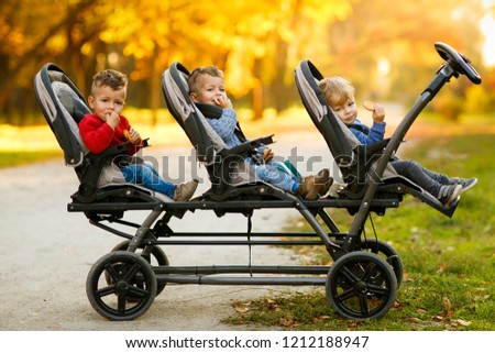 The happy triplets sit in a  baby stroller and eat cookies at autumn park Royalty-Free Stock Photo #1212188947