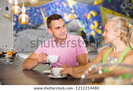 Couple of sporty people relaxing during workout at bouldering gym, drinking coffee in cafeteria

