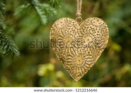 Golden yellow heart shaped ornamental decoration made of metal hanging on jute string on a Christmas tree, blurry green background