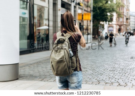 The girl on the street takes pictures of the beautiful buildings in Leipzig in Germany. She makes a street mobile photo to share it on social networks with friends.