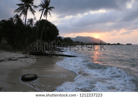 early morning sunrise shot of a beach side swimming pool with palm trees behind, mountains, the ocean with orange sunlight reflection on the wavy water surface. Beautiful Koh Phangan island, Thailand