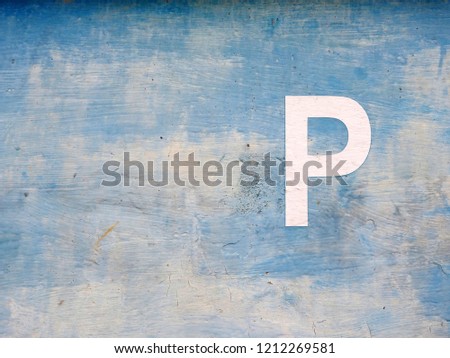 
A parking sign in the form of a white letter on a pale blue wall.					
