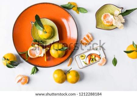 Still life with tangerines on an orange plate on a white background with a smartphone. Concept foodbloger.