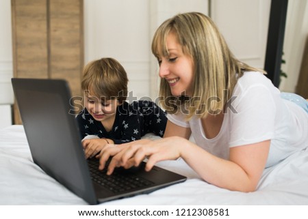 Mother and son lying on the bed in pajamas, smiling and watching cartoons on laptop.