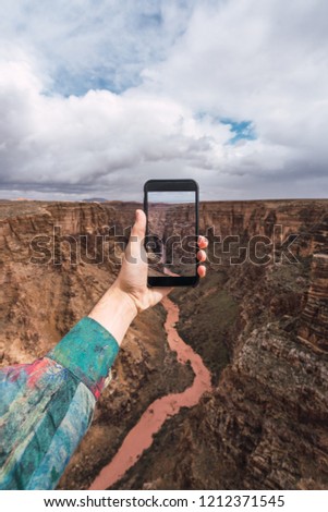 Crop hand of person in bright shirt holding smartphone and taking picture of Grand Canyon in Arizona on cloudy sky background 
