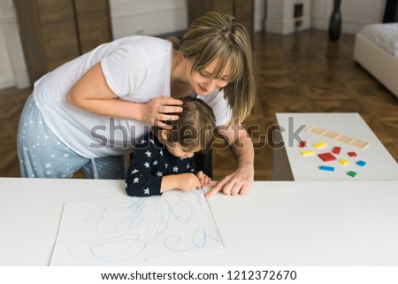 Happy smiling mom and boy drawing together on a blank paper with crayons in the living room.