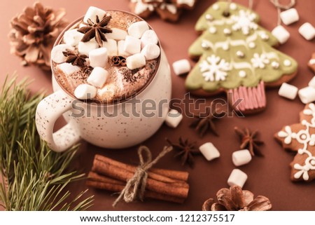 Beige mug of traditional Christmas hot chocolate or cocoa with marshmallow, traditional Christmas gingerbread, Christmas tree branches and cones on a brown solid background, close-up, top view