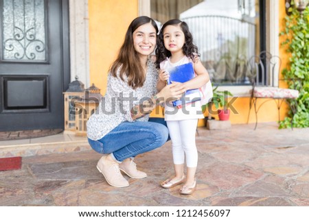 Full length portrait of cute mother and daughter with books outside house