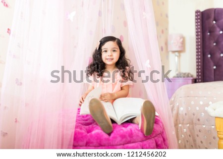 Portrait of female child viewing picture book while sitting on ottoman in princess bedroom