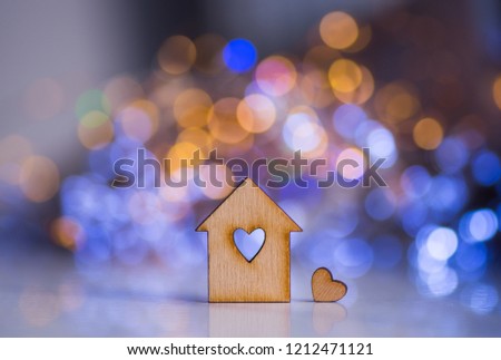 Wooden icon of house with hole in the form of heart with little heart on colorful bokeh background. Romantic card. Concept of sweet home.