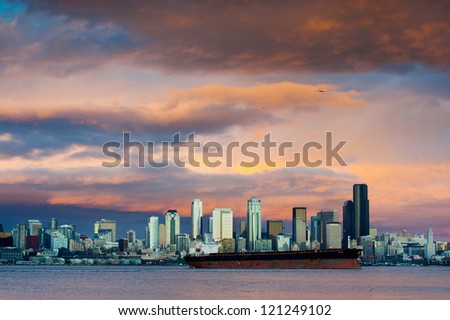 A dramatic sunset paints a beautiful sky over the Seattle, Washington skyline and Elliott Bay with a commercial ship in the foreground.