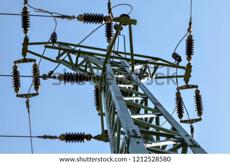 View from ground to power pylon top. Cables and ceramic isolators visible against blue sky. Abstract power industry background.
