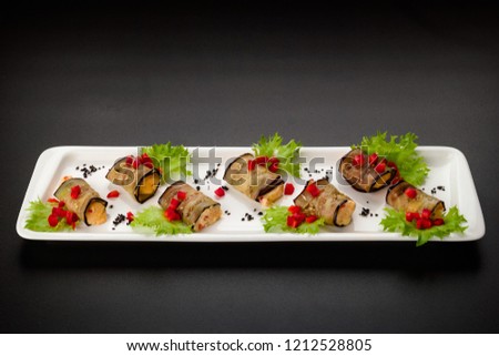 Rolls from aubergine stuffed cheese and tomato lie on a white plate, food close-up abstract background, selective focus in the center of the frame