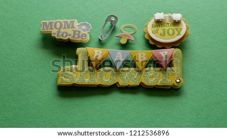 baby shower written on a colorful triangular banner with mom to be and bundle of joy written on cute buttons with pacifier and safety pin on a green background