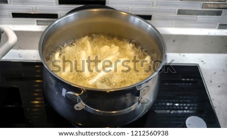 French fries in boiling oil in pot. Closeup of homemade fried potatoes in hot oil with bubbles. Fast food concept at home. Peeled, sliced and frying potatoes. Preparing dinner for friends or guests.