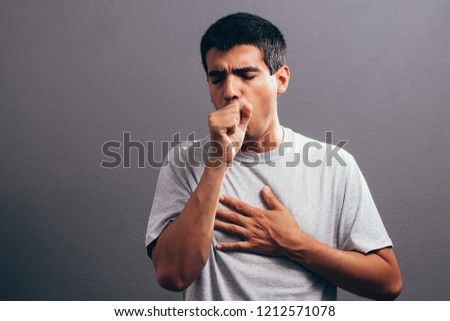 Man coughing into his fist, isolated on a gray background Royalty-Free Stock Photo #1212571078