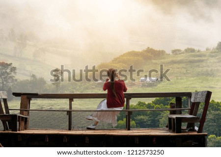 Young woman sitting on the Wooden balcony of cliff is taking photo with the smartphone on the beautiful mountains peak. Lifestyle/travel concept.