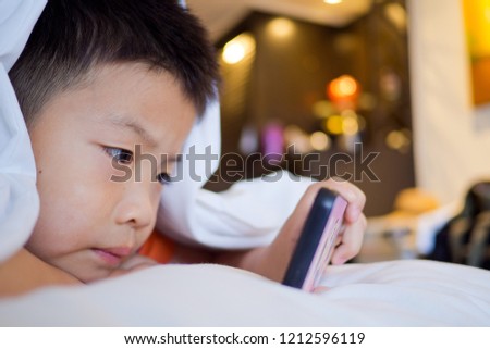 asian chinese boy playing smartphone on bed, watching smartphone, kid use phone and play game, child use mobile, addicted game and cartoon, boy play phone
