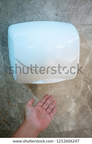 Man hand dries wet hand in modern vertical hand dryer in public restroom WC
