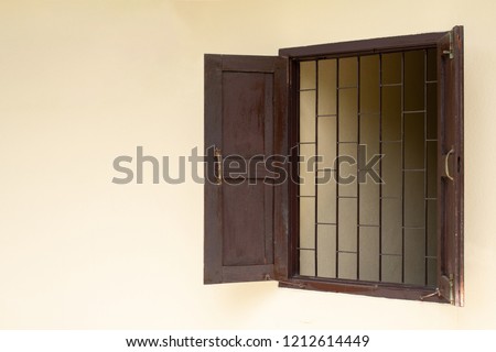 Opening wooden window with steel cage on light yellow wall, Old brown window, House protection concept