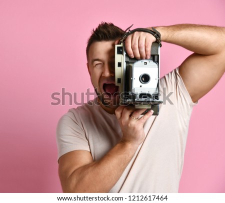 Young man take photo use antique old portable photo camera medium frame on light pink screaming background