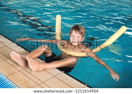 Little boy with swimming noodle in indoor pool