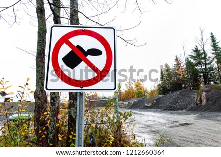 Do not litter white and red road sign in front of a construction site with gravel and rock piles - 2/2 - Closeup picture taken from the side of the road