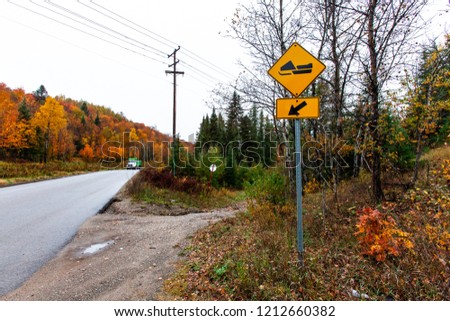 Snowmobile track to the left yellow road sign as seen from the side of a road with a truck coming - Picture taken in Quebec, Canada, while autumn colors were very present.