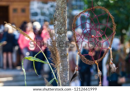 Small dreamcatcher is hanging in a tree in front of a crowd waiting to enter in the church as part of a native arts festival - 2/2 - Closeup picture with blurry people in the background