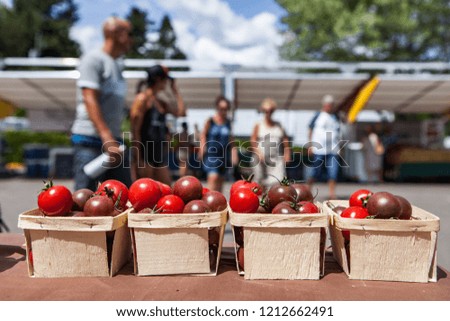Cherry tomatoes for sale in small baskets at the farmer's market with blurry food stalls and people in the background - Closeup picture with vibrant colors