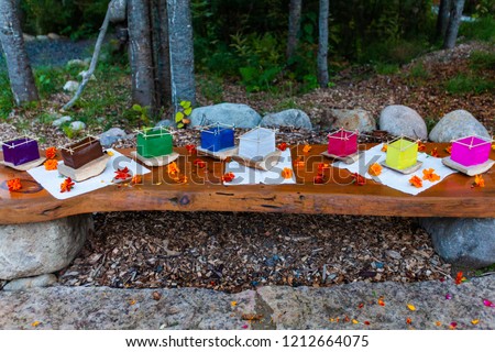Various colors of silk lantern boats mounted on cedar wood and surrounded by orange flowers on a wooden bench - 4/5 - Wide angle picture taken outside in northern Quebec