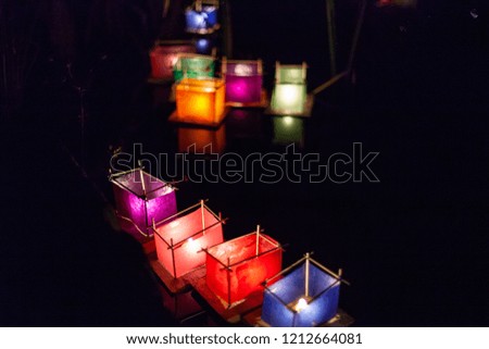 Various colors of silk lantern boats with lit candles inside, floating in a sacred pond at night - 1/3 - Picture taken outside at night in Quebec, Canada