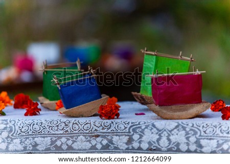 Various colors of silk lantern boats mounted on cedar wood and surrounded by orange flowers on a wooden bench - 2/5 - Closeup picture taken outside with a blurry background