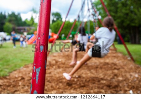 Closeup picture of a swing holder pole in a park for kids. Kids swigning in the blurry background - Picture taken on a warm summer day, with mulch ground instead of sand