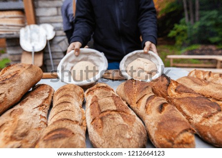 Man is showing 2 ready to cook bread doughs, while standing behing a table full of freshly cooked loaves of bread - Pictures taken during a bread and pizza making workshop