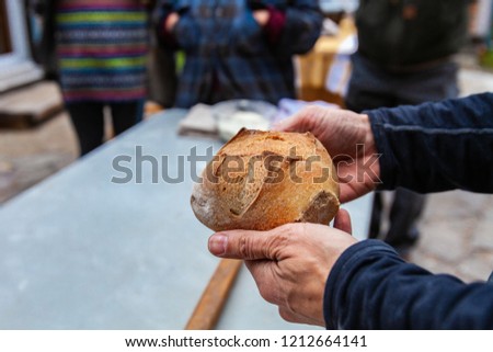 Man is holding a small loaf of bread that just came out of an outdoor bread oven, with people around looking - Pictures taken during a bread and pizza making workshop