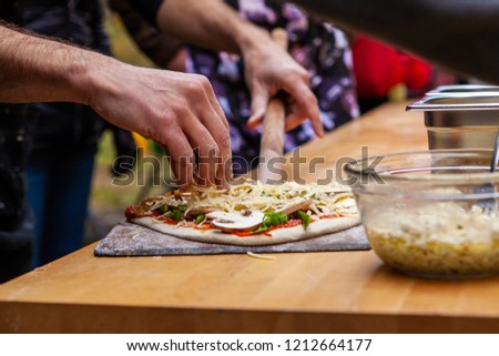Man is adding dressings on his freshly kneaded pizza dough, right before putting it into an outdoor bread oven - Pictures taken during a bread and pizza making workshop