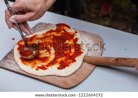 Man is spreading tomato paste on freshly kneaded pizza dough, before putting it into an outdoor bread oven - Pictures taken during a bread and pizza making workshop
