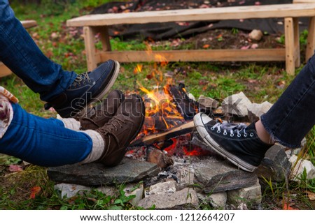 3 pairs of feet warming up their shoes around a camp fire outdoors in autumn - wide angle - Pictures taken during a bread and pizza making workshop with many people from all ages and generations.