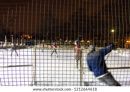 Kids playing outdoor hockey on ice at night in a park of Quebec, Canada - 2/3 - As seen from behind the rink's protective net