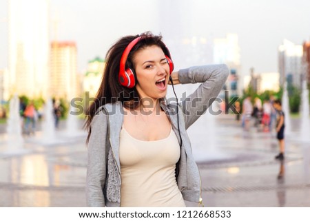 Girl listening to music streaming with headphones and winking on the street.
