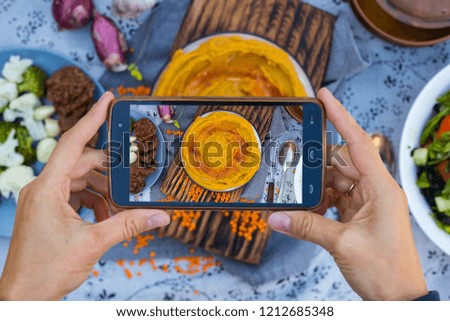Smartphone photography of food. Woman hands holds mobile phone and take or make beautiful trendy food photo for social networks or blogging. Israeli chickpea hummus dip