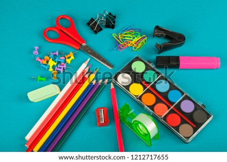 Close up picture of colored school supplies - Scissors, marker, pencils, gouache, etc. on blue background