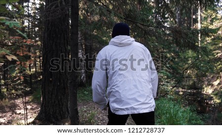 Young man on camping trip. Concept of freedom and nature. View of man from back walking in woods along path on sunny autumn day