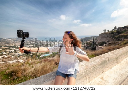 Beautiful young woman with a camera in her hands, traveler and bloggen taking selfie on a background of beautiful landscape with mountains and sea